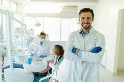 Male dentist standing with his hands crossed  wearing gloves and white coat and looking at camera.