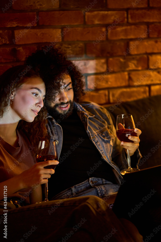 married couple watching movie on laptop, relaxing and watching movies at home, having rest after hard week, sit drinking wine, copy space. romantic time
