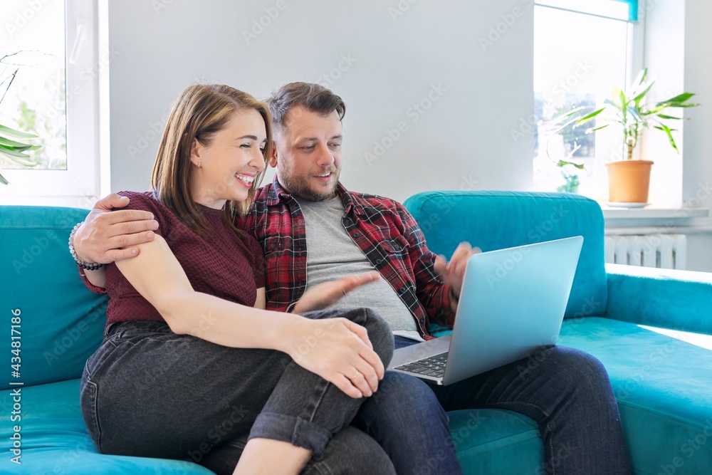Happy middle aged couple sitting on couch with laptop