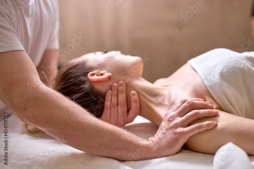 Professional cropped therapist doing healthy massage on neck and shoulders to female client lying on back  side view. at spa salon