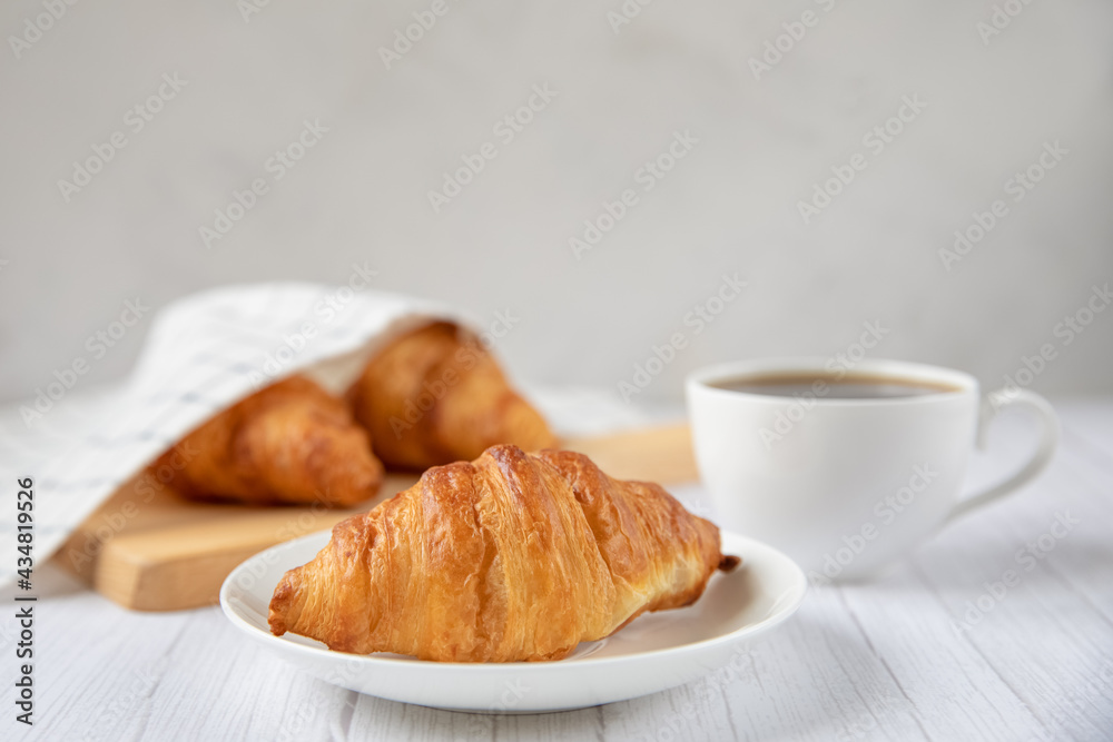 Concept food. Delicious fresh croissants on a plate and a cup of coffee next to. Light background.