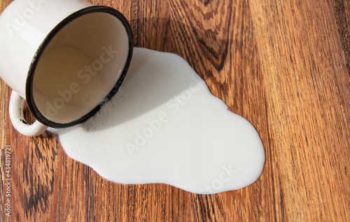 metal mug with milk, fell on the floor spilling milk with a stain on the wooden floor, trouble