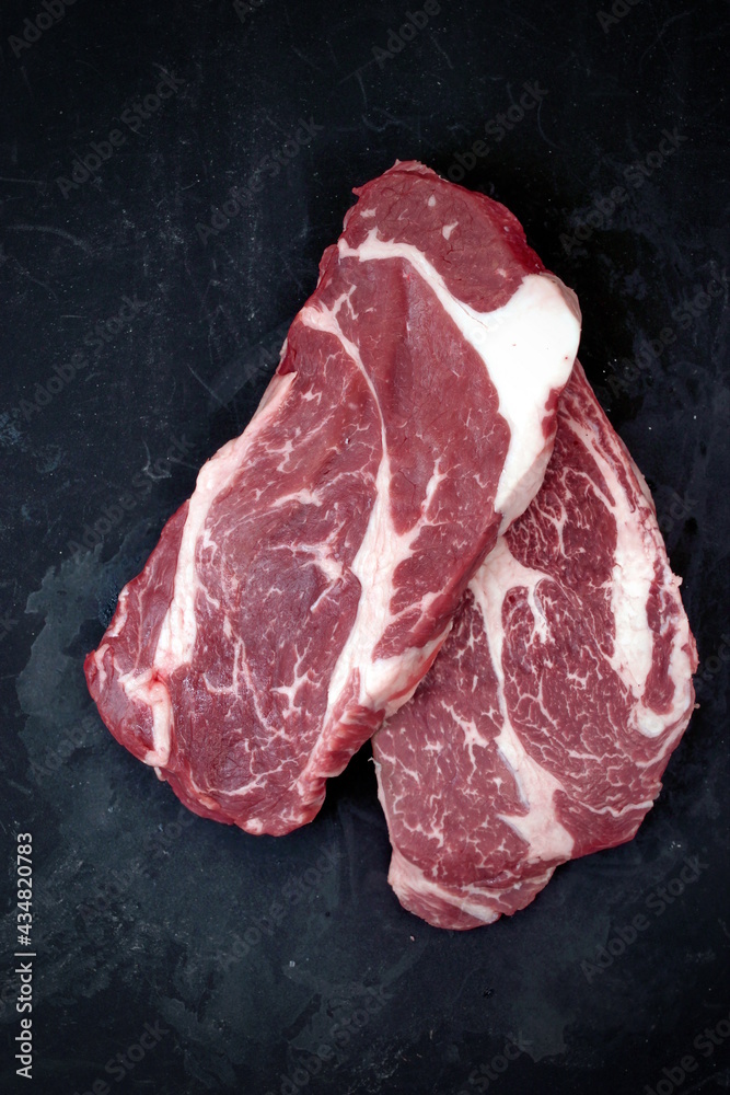 Raw Steak. Sirloin Raw Beef Steak, Overhead View. Single Raw Striploin Steak from Marbled Beef on Black Background. Black Angus Beefsteak Meat. Raw Sirloin Cut. Uncooked Prime Beef Steak.
