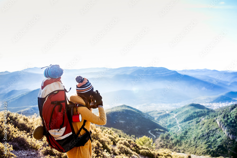 Girl hiker with backpack taking a picture of the mountain scenery. Travel lifestyle concept.	