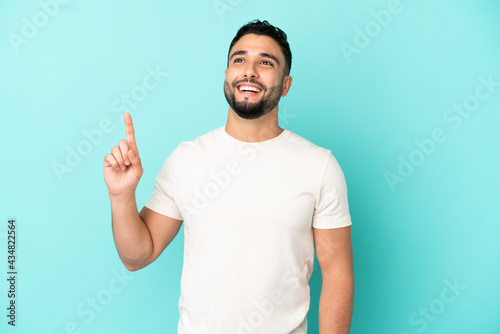 Young arab man isolated on blue background pointing up and surprised