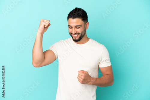 Young arab man isolated on blue background celebrating a victory