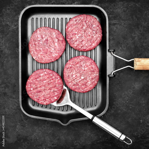 Raw Steak Burgers Cutlets On Grill Pan. Burgers Patties from Marbled Beef Meat in Frying Pan on Black Background, Overhead View. Griddle Pap and Ground Beef Meat Patties for Grilling, Top View.