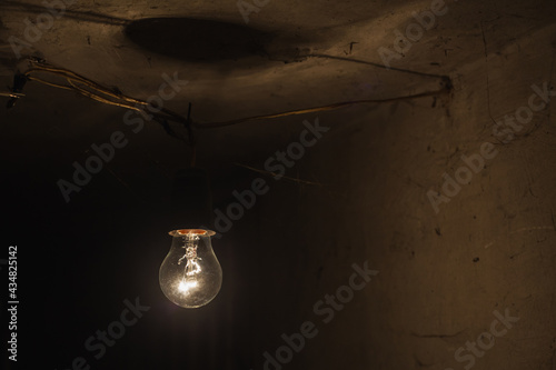 Old tungsten bulb. The incandescent lamp with a tungsten filament wobbles on the wire. Light from a light bulb. Light bulb close-up covered with cobwebs. photo