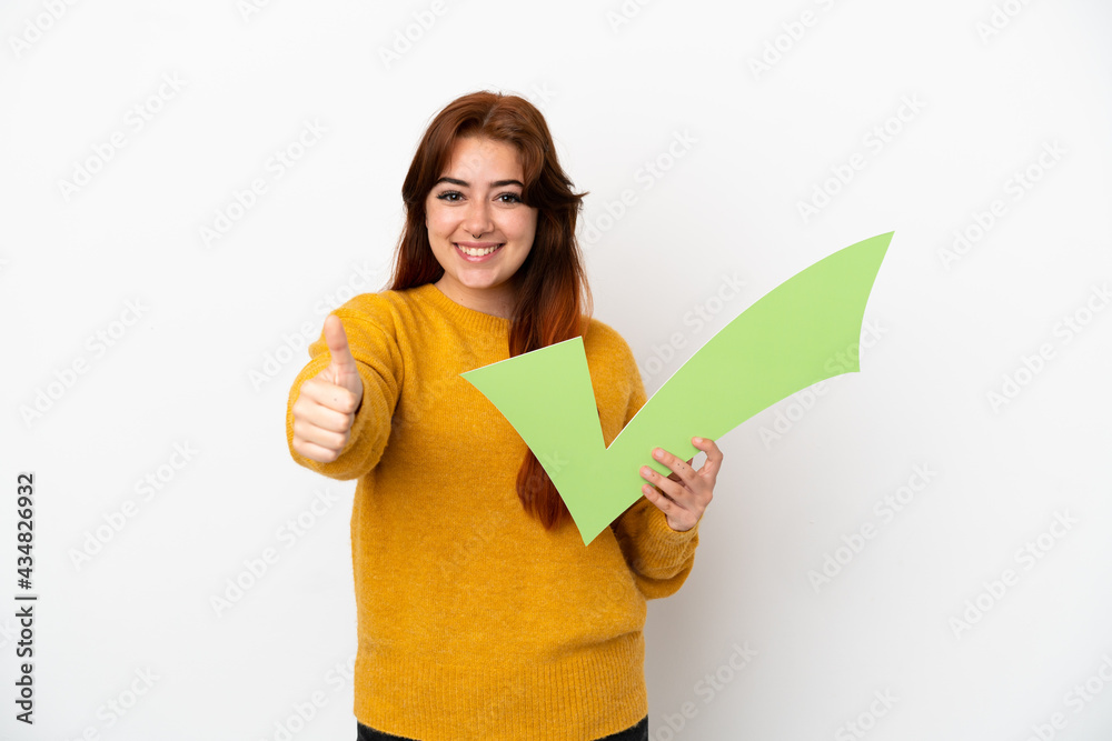 Young redhead woman isolated on white background holding a check icon with thumb up Young redhead woman isolated on white background holding a check icon with thumb up