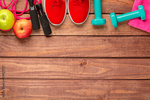 Fitness and sport concept. Red sneakers, apples, jump rope, dumbbells and pink towel on wooden background. Free space