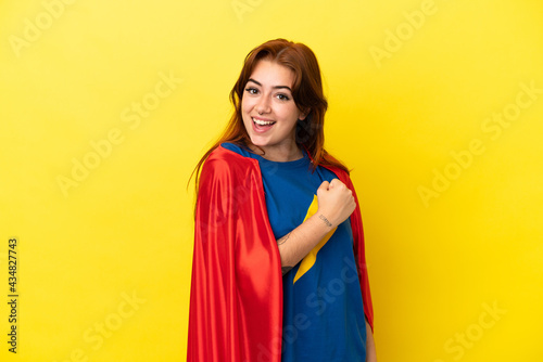 Super Hero redhead woman isolated on yellow background celebrating a victory