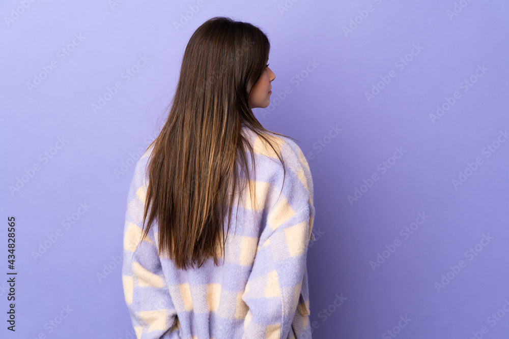 Teenager Brazilian girl over isolated purple background in back position and looking back Teenager Brazilian girl over isolated purple background in back position and looking back