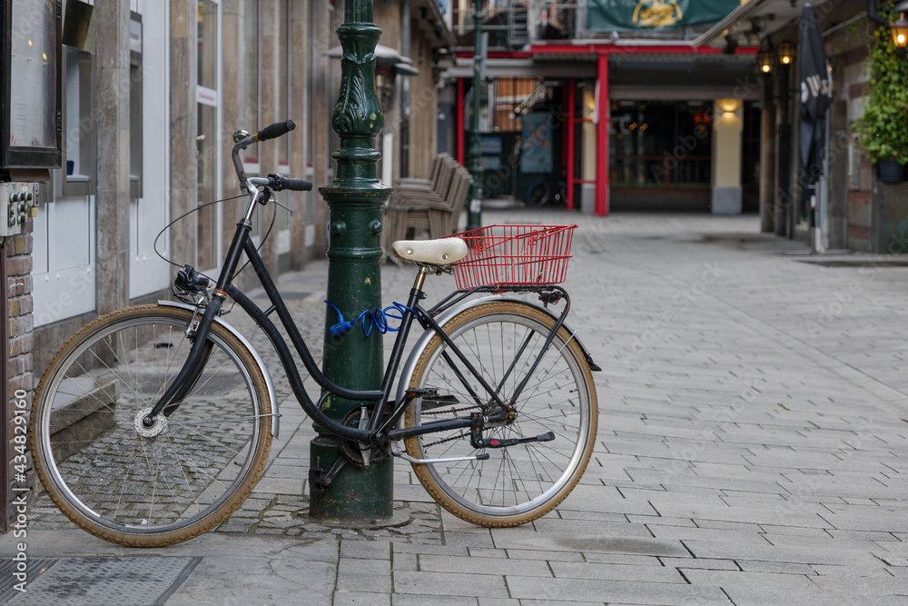 Urban Cycling city lifestyle concept. Selective focus view at bicycle lock on street lighting pole on the sidewalk with blur background of empty walking street. Urban Cycling city lifestyle concept. Selective focus view at bicycle lock on street lighting pole on the sidewalk with blur background of empty walking street.