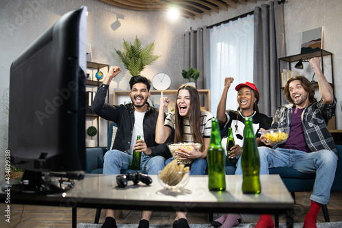 Emotional men and women geturing with fists during victory of favorite football team. Four diverse friends watching match on TV while staying at home. Entertainment concept. photo