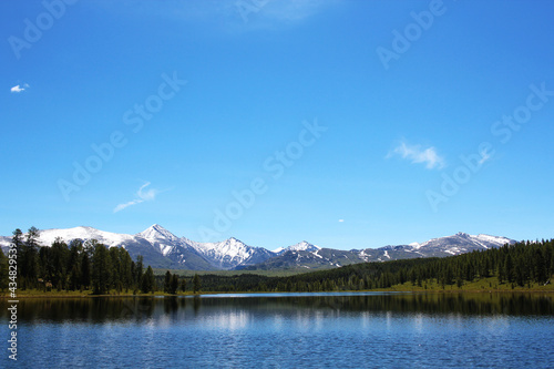 A bright blue lake surrounded by forest and snow-capped mountains. A pastoral, soothing picture of pristine nature. Mountain Altai. The nature of Russia