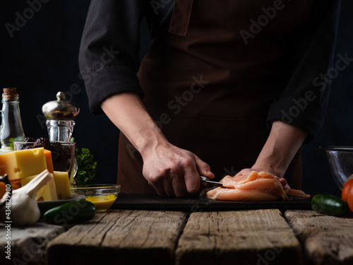 The cook will make minced meat from raw meat. The photo shows the process of cutting meat. Rough wooden table. Nearby is soy sauce, salt, spices. Dark background. photo