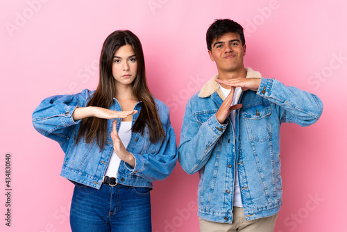 Fotografie Young couple over isolated pink background making stop gesture with her hand to