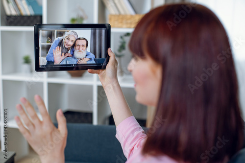 Young woman waving hand during video chat with lovely grandparents on digital tablet. Connection of family during pandemic. Technology concept.