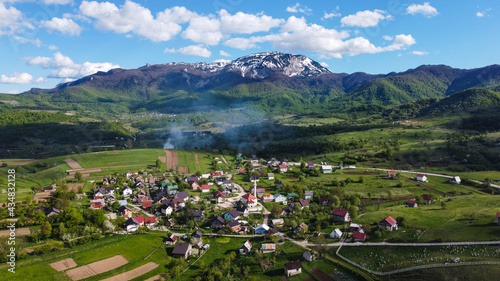 Idyllic mountain landscape in spring. Aerial drone view of a small village, green hills and mountains in the background.	 photo