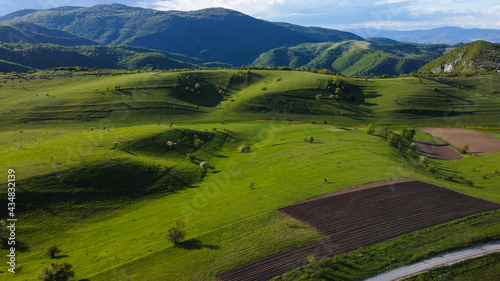 Aerial drone view of green hills and patterned fields on mountain. Beautiful grassy hills at sunset. Meadow and pasture. 