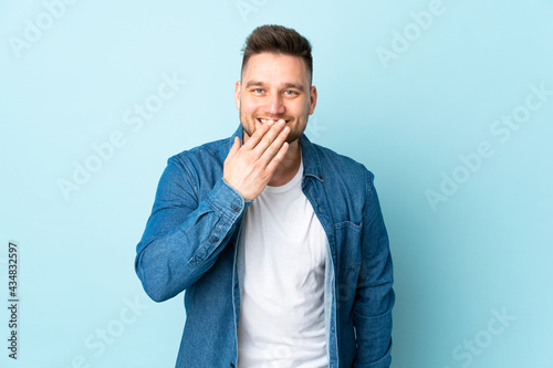 Russian handsome man isolated on blue background happy and smiling covering mouth with hand