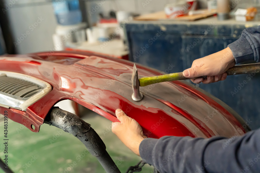 Sheet metal worker hammers the bumper of a vehicle. Madrid.
