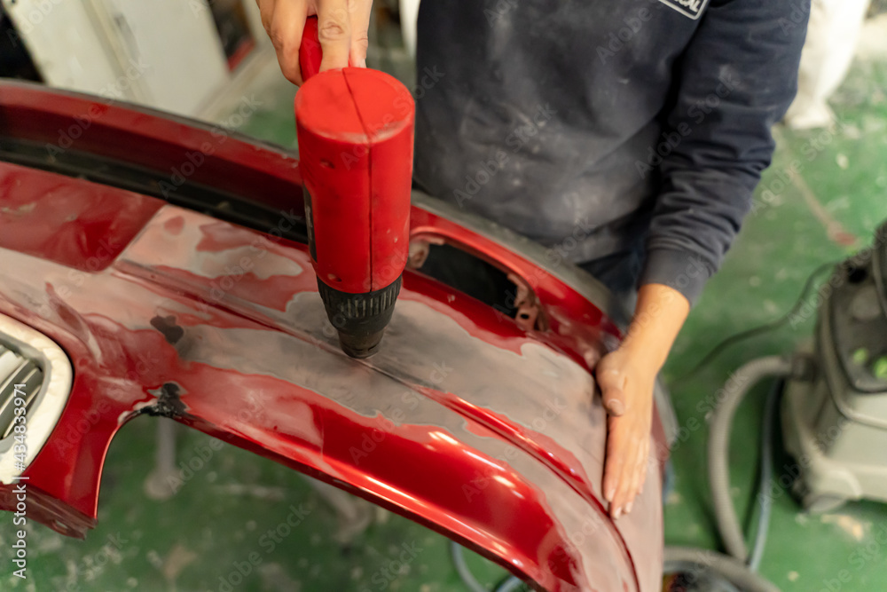 Workshop worker molds bodywork with heat gun. Madrid,