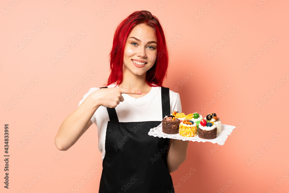 Pastry chef holding a muffins isolated on pink background holding copyspace imaginary on the palm to insert an ad Pastry chef holding a muffins isolated on pink background holding copyspace imaginary on the palm to insert an ad