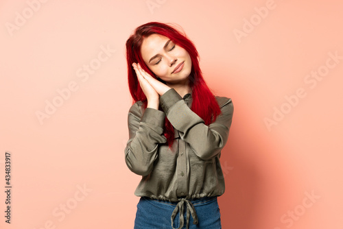 Teenager red hair girl isolated on pink background making sleep gesture in dorable expression