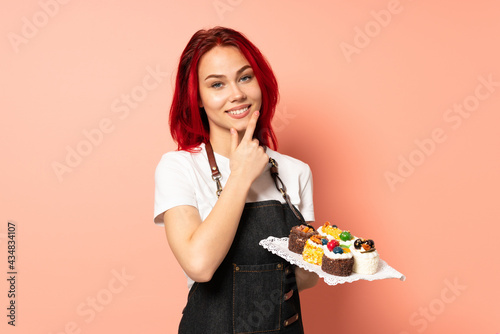 Pastry chef holding a muffins isolated on pink background happy and smiling