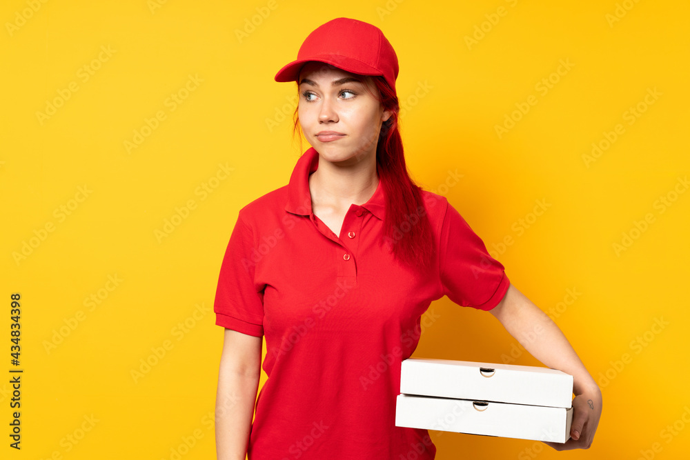 Pizza delivery girl holding a pizza over isolated background making doubts gesture looking side Pizza delivery girl holding a pizza over isolated background making doubts gesture looking side