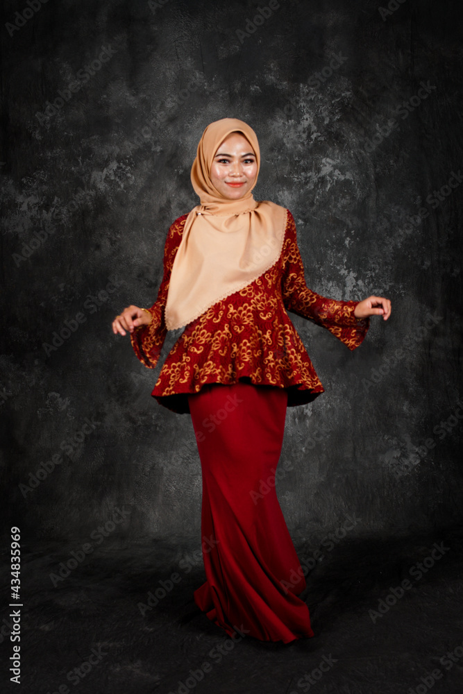 Portraiture of beautiful young Muslim girl wearing hijab and dress known as Baju Kurung Moden. Fashion for dinner, event and feast day. Studio shot with a black oil painting background. Portraiture of beautiful young Muslim girl wearing hijab and dress known as Baju Kurung Moden. Fashion for dinner, event and feast day. Studio shot with a black oil painting background.