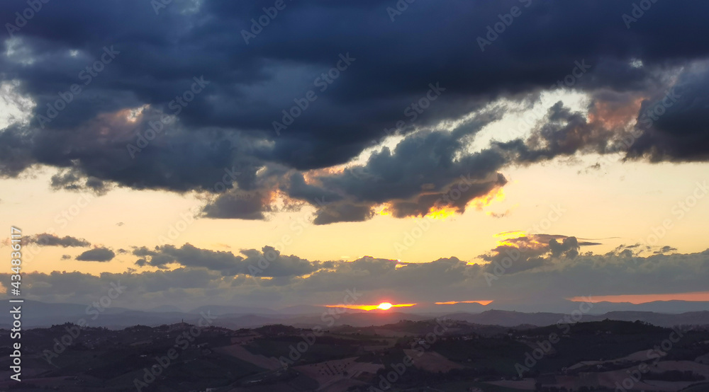 Il sole tramonta dietro alle nuvole sopra le montagne le colline e le valli dell’Appennino
