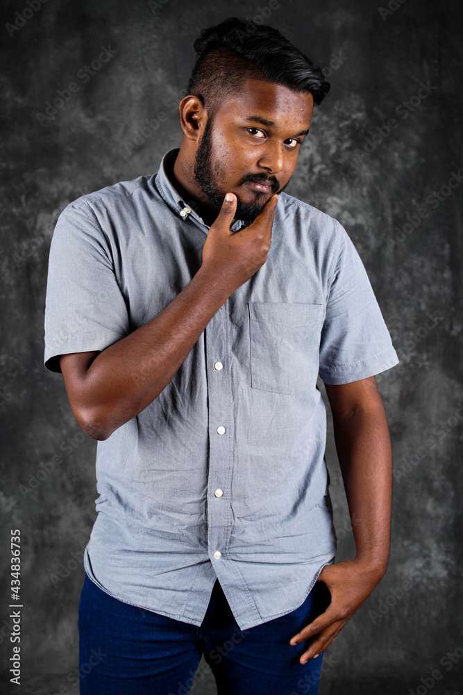 Portrait of a bearded Indian man with an intense look standing with a black background.