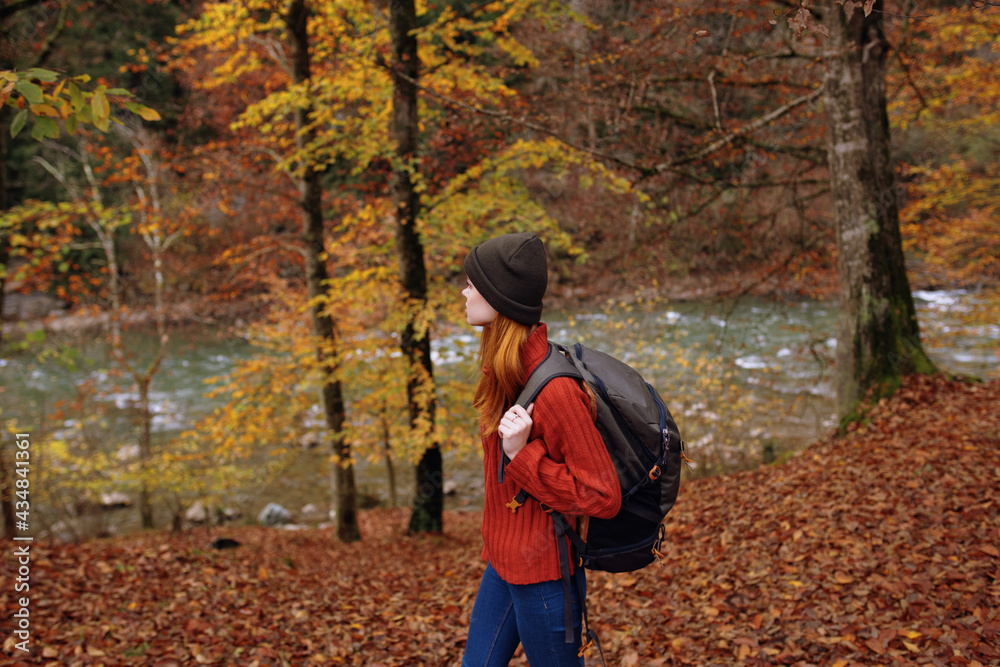 side view of happy woman in park in autumn near river and backpack on her back