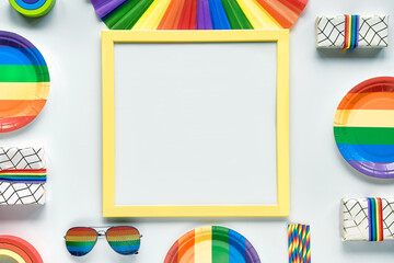 LGBTQ pride month decor, mockup with copy-space, text place. Rainbow pattern objects on off white background. Party paper plates, drink straws, sunglasses, fan, wooden toy. Flat lay, top view.