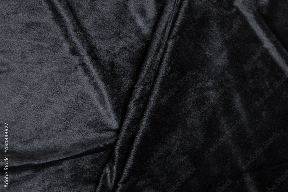 Fototapeta premium Colored black textile satin fabric folded in folds and waves with highlights and texture