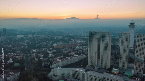 Aerial drone hyperlapse of the business and financial district of Santa Fe in Mexico City at sunrise, with skyscrapers and the cityscape. Popocatepetl active volcano in the background with an eruption photo