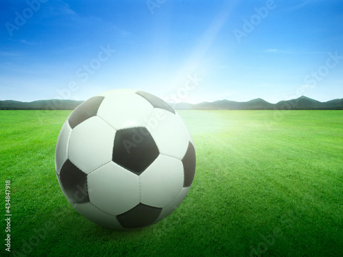 Traditional soccer ball on background image of lush grass field under blue sky