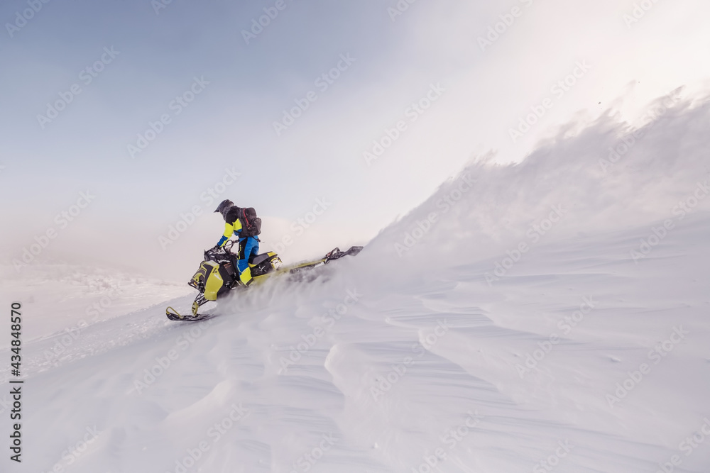 Snowmobile female rider riding on beautiful mountain slope