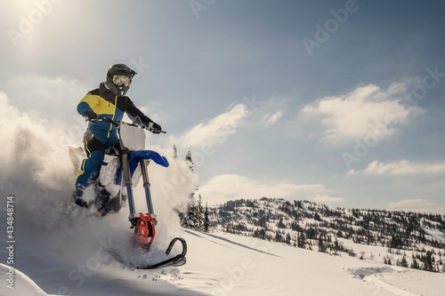  Rider on snowbike in beautiful mountain landscape, puffs of snow behind motorcycle