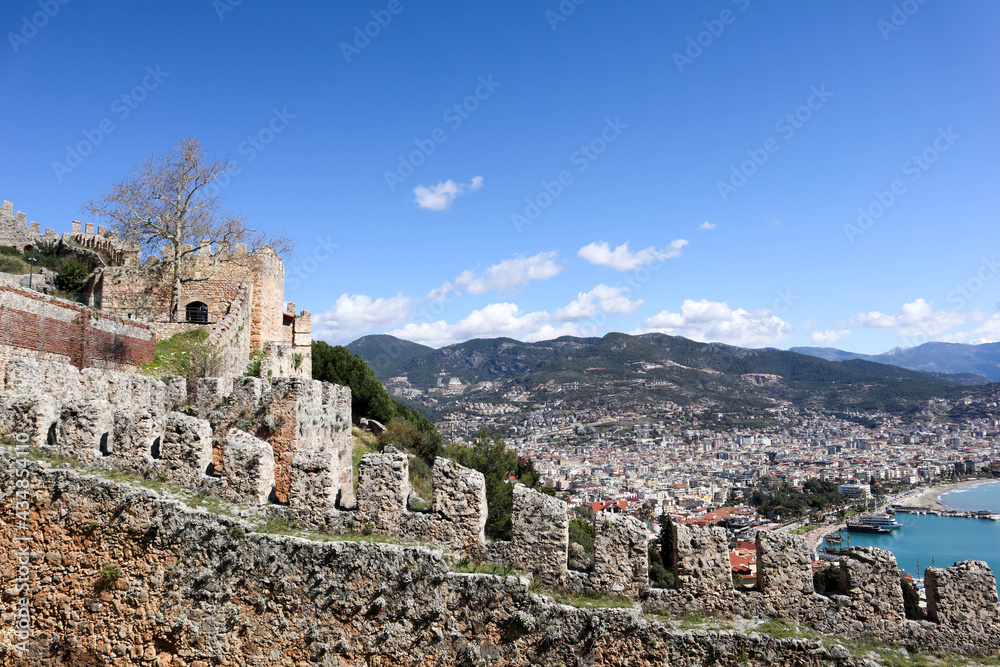 wall with battlements of medieval old Alanya fortress in Turkey with azure mediterranean sea, city and mountains on the background