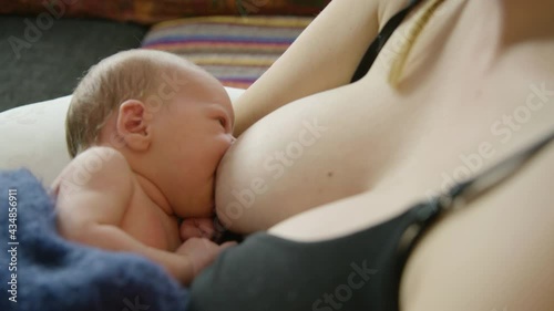 A newborn baby breastfeeds in a quiet setting at home, close up forward
