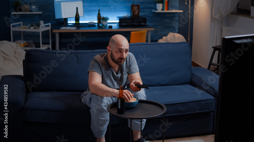 Football sport watching game late at night eating popcorn, cheering beer bottle for favourite winner team. Man enjoying championship entertainment match soccer fan looking at competition on television