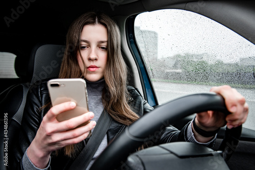 Young woman using mobile phone while driving car on bad weather condition.