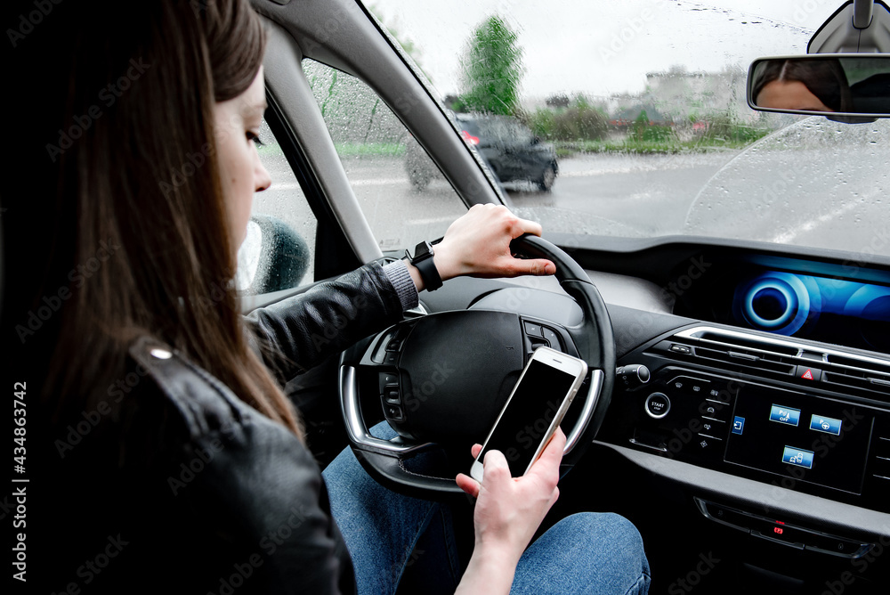 Young woman using mobile phone while driving car on bad weather condition. Young woman using mobile phone while driving car on bad weather condition.
