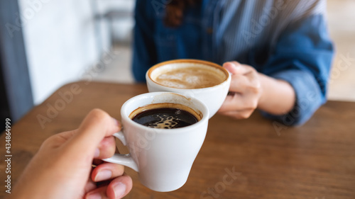 Closeup image of a woman and a man clinking coffee cups together in cafe