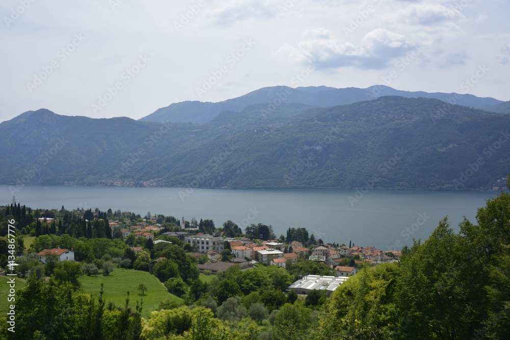 Panorama of mountain lake Como with village by waterfront surrounded by green hills covered with cedar forest. Italy Lierna, June 23 2018.