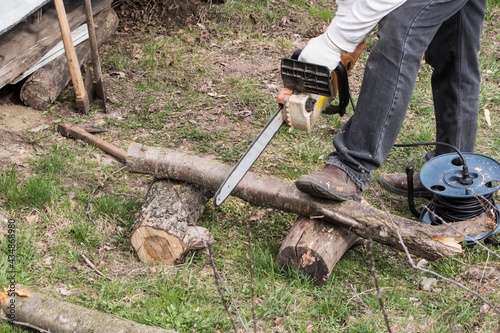 A man with an electric saw saws a tree for firewood in the garden