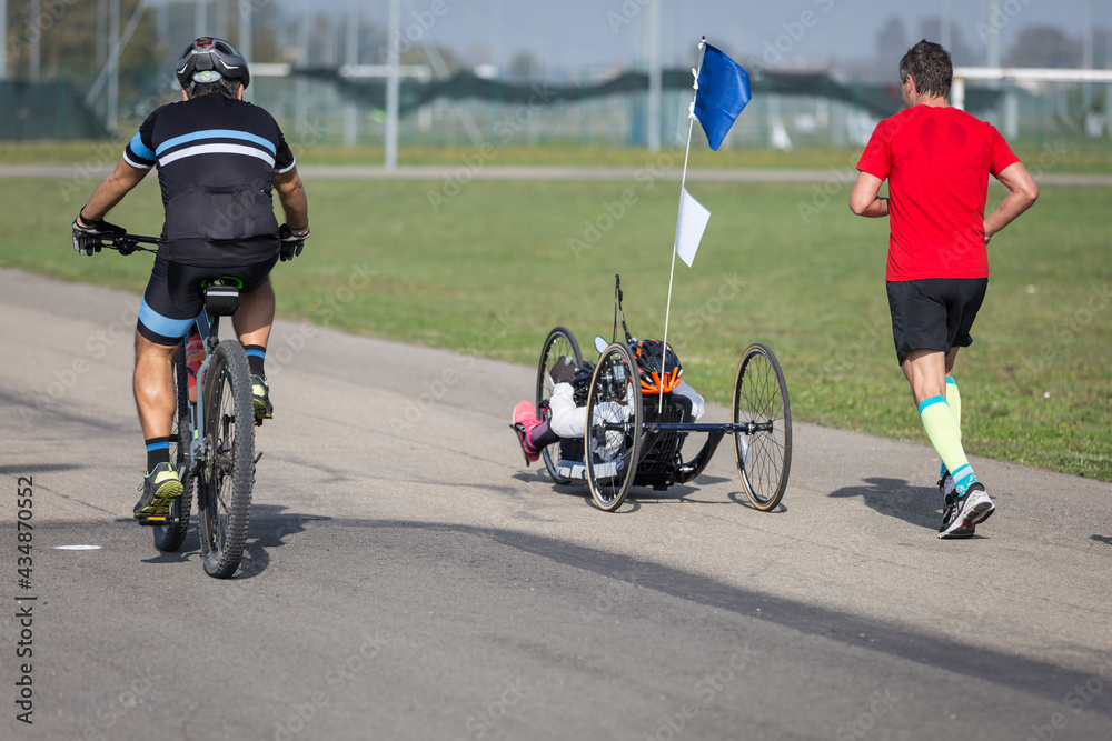 Fototapeta premium Disabled Athlete who Trains with her Hand Bike with Cyclist and Runners at her Side